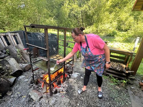 Kobieta piecze placki na ruszcie nad ogniskiem w zielonym ogrodzie CuratioW podczas letniego grillowania w Rajczy