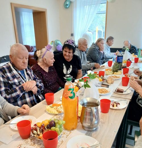 Seniorzy przy długim, zastawionym stole podczas wspólnego urodzinowego poczęstunku w CuratioW w Rajczy