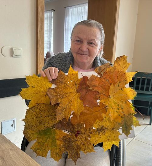 Seniorka trzyma jesienną kompozycję z żółtych i pomarańczowych liści klonu wykonaną w CuratioW w Rajczy