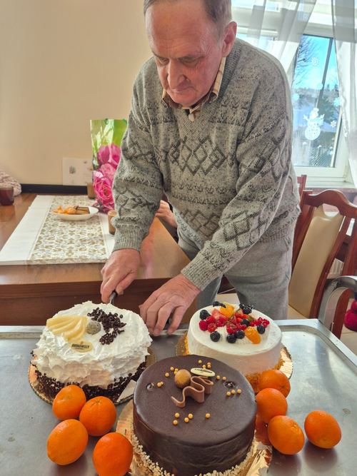 Senior kroi trzy ozdobne torty z owocami i mandarynkami podczas uroczystości w CuratioW w Rajczy