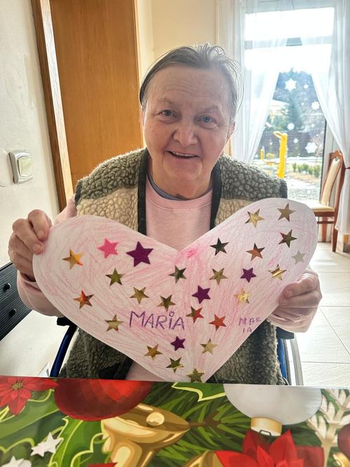 Uśmiechnięta seniorka trzyma własnoręcznie ozdobione papierowe serce w gwiazdki z napisem imienia w CuratioW