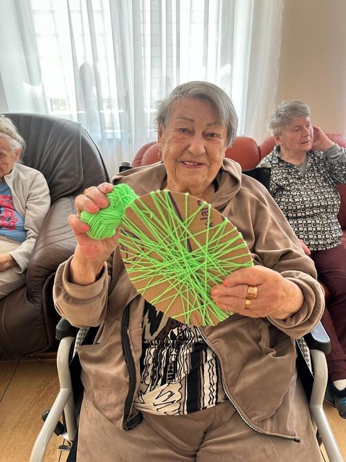 Uśmiechnięta seniorka trzyma okrągłą mandalę z zielonej nawiniętej włóczki, zajęcia rękodzielnicze CuratioW w Rajczy