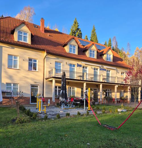 Tylna elewacja CuratioW z trawnikiem, sprzętem siłowni plenerowej i parasolami na tarasie