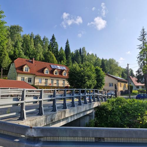 CuratioW w Rajczy latem, betonowy most i bujna zieleń pod błękitnym niebem z chmurami