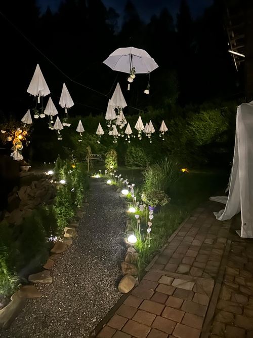 Wieczorna iluminacja ogrodu CuratioW w Rajczy, podświetlone białe parasolki i lampki wzdłuż ścieżki w nocy