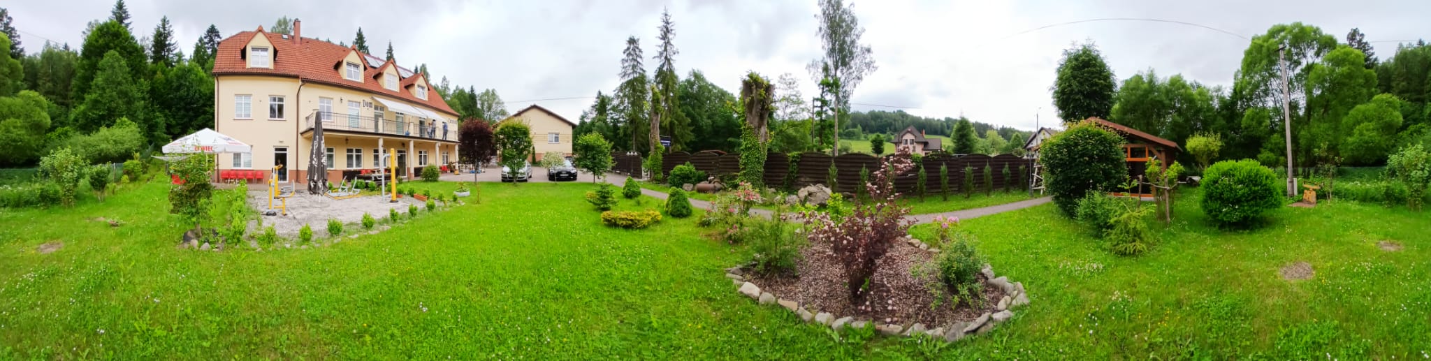 Panorama posesji Domu Aktywnego Seniora CuratioW w Rajczy — budynek, ogród z iglakami, altana i siłownia plenerowa na tle Beskidu Żywieckiego