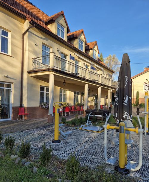 Żółta fasada budynku CuratioW z balkonem i tarasem, siłownia plenerowa na żwirze w słońcu